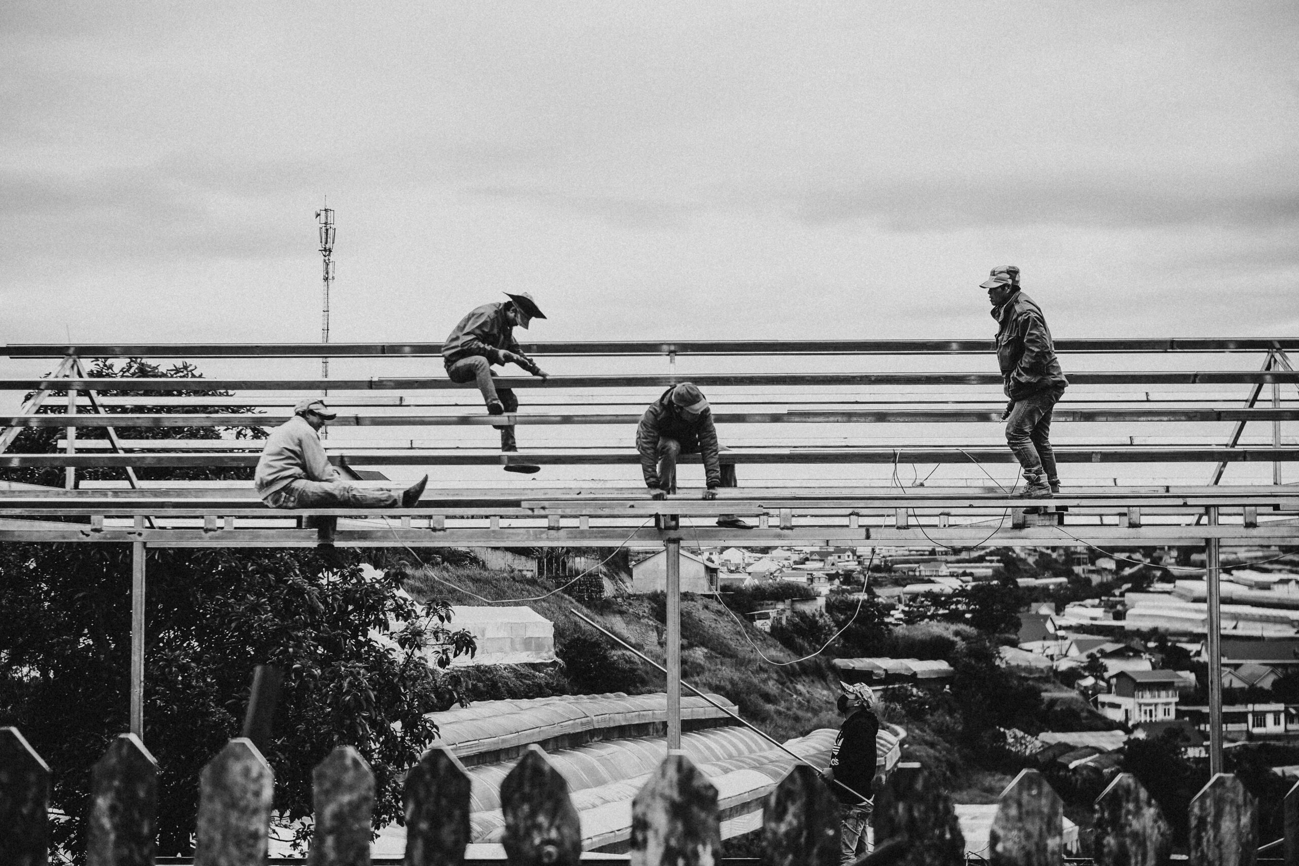 Black and white image of workers on a metal framework with a city backdrop.