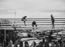 Black and white image of workers on a metal framework with a city backdrop.