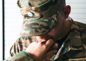 A military officer in camouflage receiving a respectful hand kiss indoors.