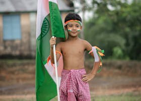 A young boy celebrates Indian Independence Day holding the national flag outdoors in Agartala.