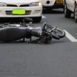 A motorcycle lies on a city road amidst traffic, indicating a recent accident.