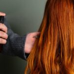 Close-up of hairdresser spraying hair product on long red hair. Hair Fall Remedies
