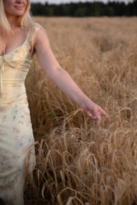 Woman in a floral dress touches wheat in a serene summer field setting.